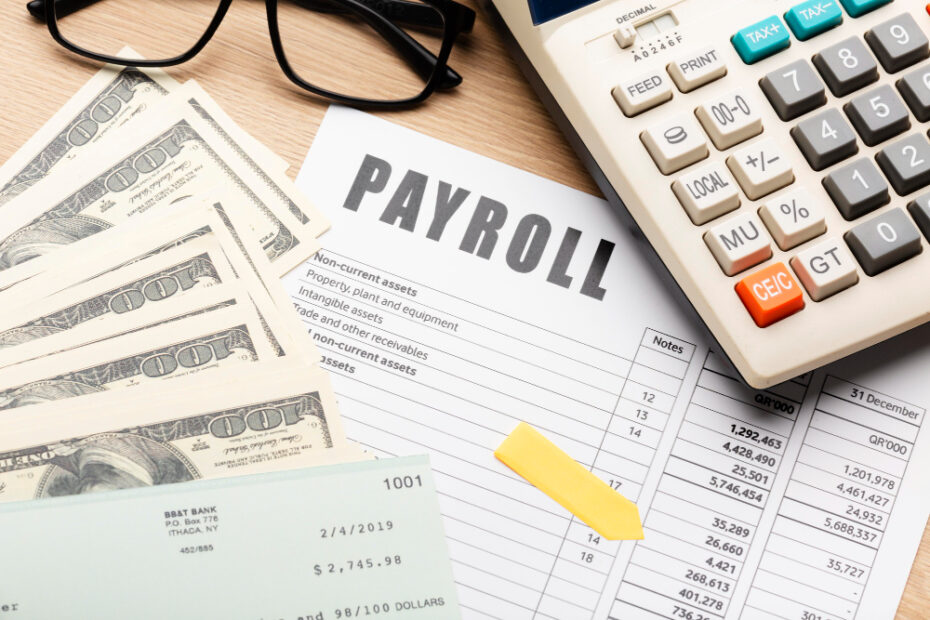 الصورة تعرض مشهدًا لمكتب محاسبة أو إدارة موارد بشرية، حيث يظهر نموذج كشوف الرواتب (Payroll) بشكل بارز على الطاولة، ويحيط به حزمة من النقود، وآلة حاسبة تستخدم لحساب الرواتب والضرائب المرتبطة بها. كما يتضمن المشهد شيكًا مصرفيًا يعكس عملية دفع الرواتب للموظفين. الصورة تعبر عن عمليات إدارة الرواتب بشكل احترافي وتوضح أهمية التوثيق الدقيق والإدارة المالية المنظمة في الشركات.