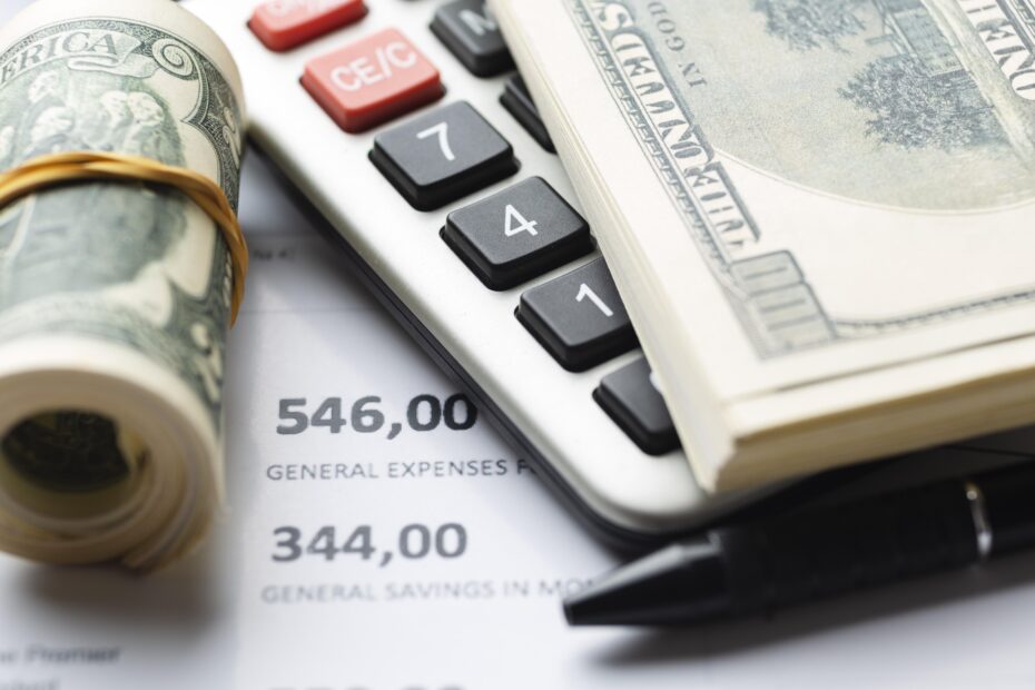 عرض الصورة مشهدًا ماليًا احترافيًا يتضمن آلة حاسبة، رزمة من النقود الورقية، ومستندات محاسبية بأرقام مالية واضحة. يعكس هذا المشهد جوهر الأعمال المتعلقة بالإدارة المالية والضرائب. ترمز الصورة بوضوح إلى العمليات الدقيقة التي يعتمد عليها المحاسبون ورجال الأعمال أثناء حساب القيمة المضافة، حيث تمثل الأرقام والأدوات المالية الأساس لضمان دقة العمليات الحسابية وتحقيق الامتثال الضريبي الكامل.